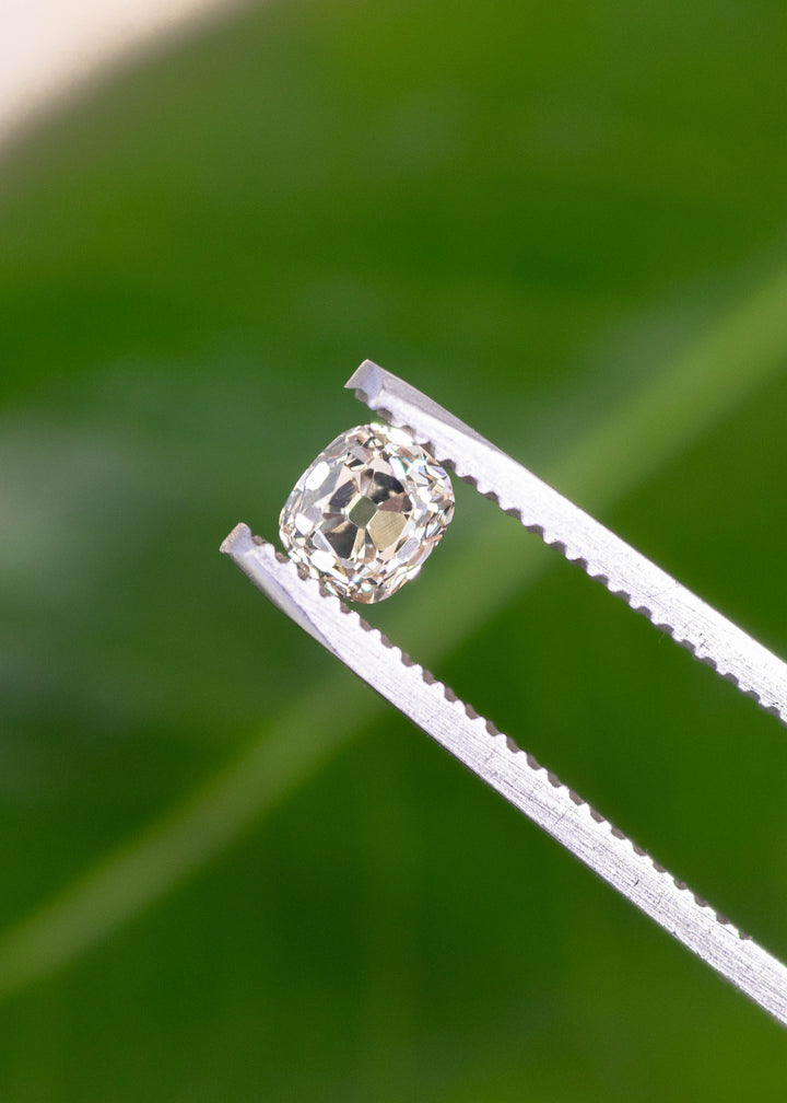 Old mine cut cushion diamond held in tweezers showing chunky facets and vintage cut structure.