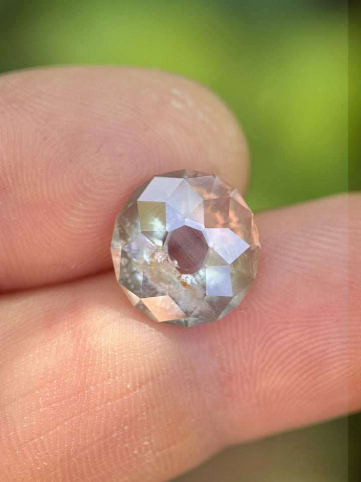 Natural unheated 6.38ct Umba River sapphire with modified Portuguese cut shown on fingertips under natural light, revealing pastel gray-green tones