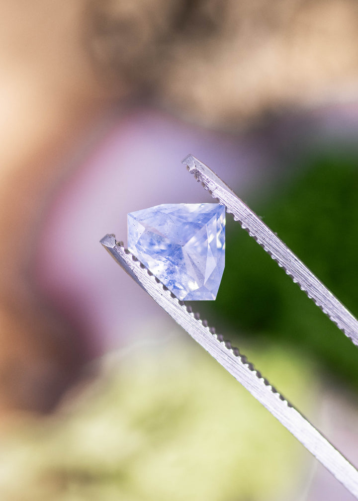 Loose opalescent blue sapphire from Sakaraha Madagascar held in tweezers highlighting the geometric shield mixed cut and milky blue tones.