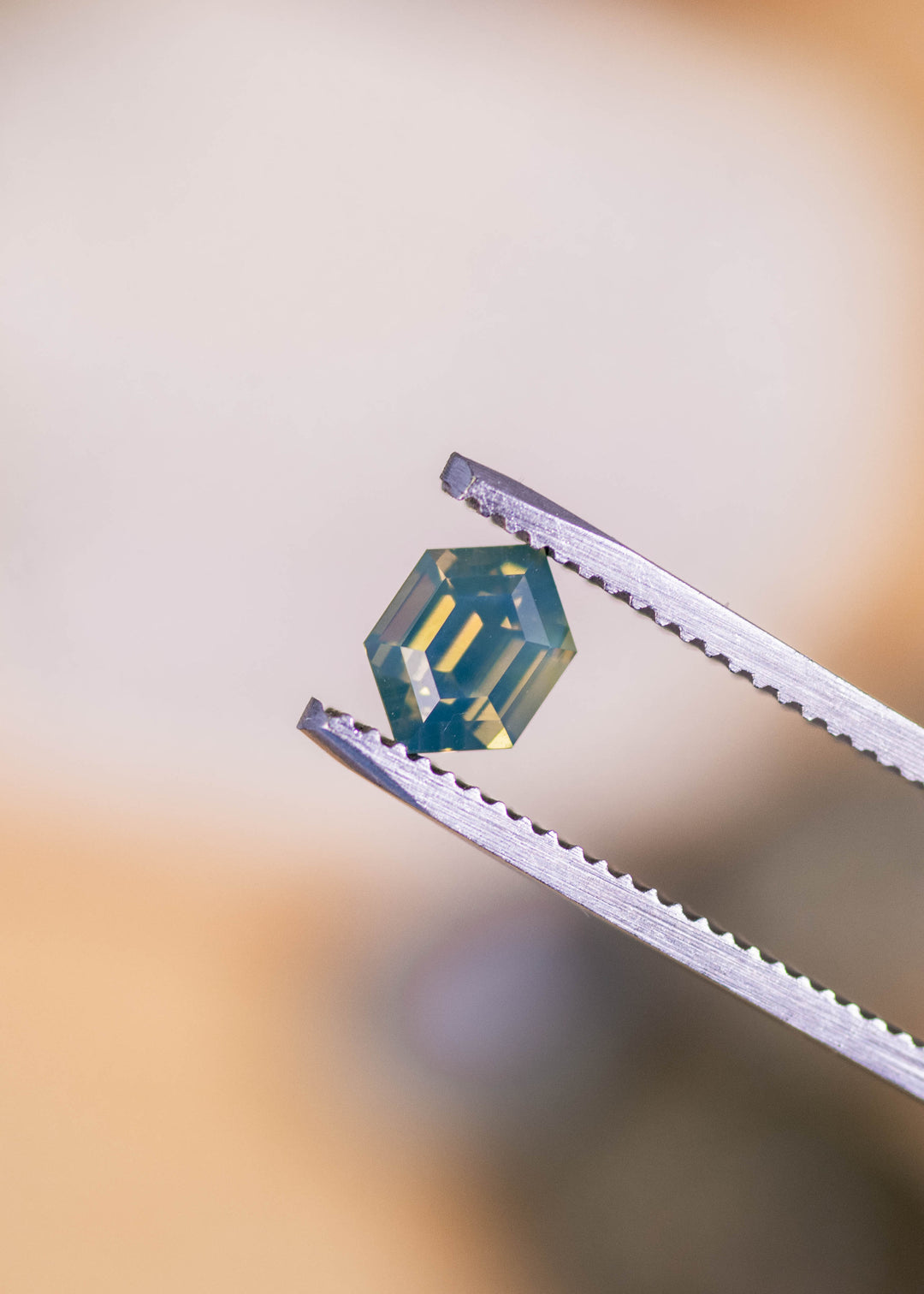 Loose opalescent green yellow sapphire from Madagascar held in tweezers displaying the hexagonal modified step cut and the gem’s soft opalescent glow.