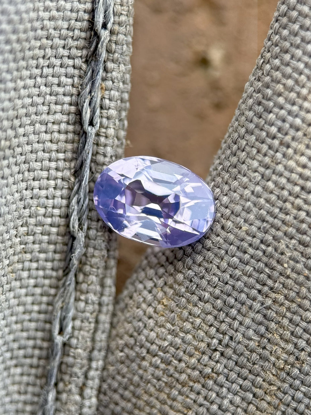 Lavender and violet 1.18ct sapphire resting on gray woven fabric, showing brilliant bi-color play