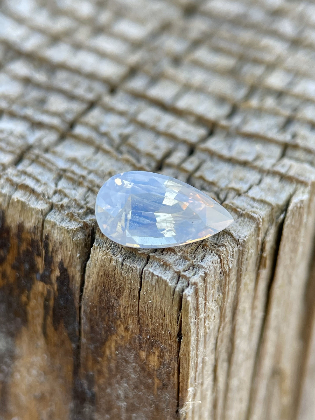 1.18-carat opalescent peach sapphire resting on rustic wood surface.