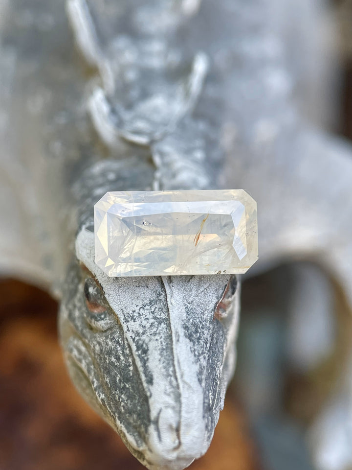 A stunning opalescent white and yellow sapphire, weighing 4.18 carats, in an elongated radiant cut, displayed on a textured backdrop. This gem is ethically sourced from Sri Lanka.