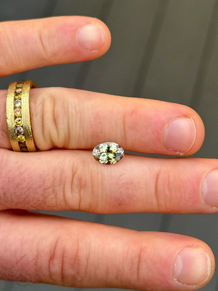 Natural-light view of a 1.98-carat Tanzanite showing yellow, teal, and green color zoning while resting on a hand, featuring its untreated custom mixed oval cut from Merelani Hills, Tanzania.