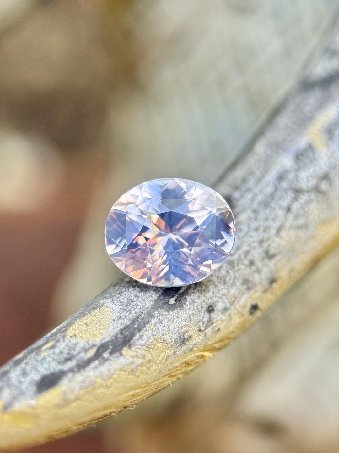 1.60-carat Sri Lankan sapphire with blush, lavender, and platinum colors resting on textured wood