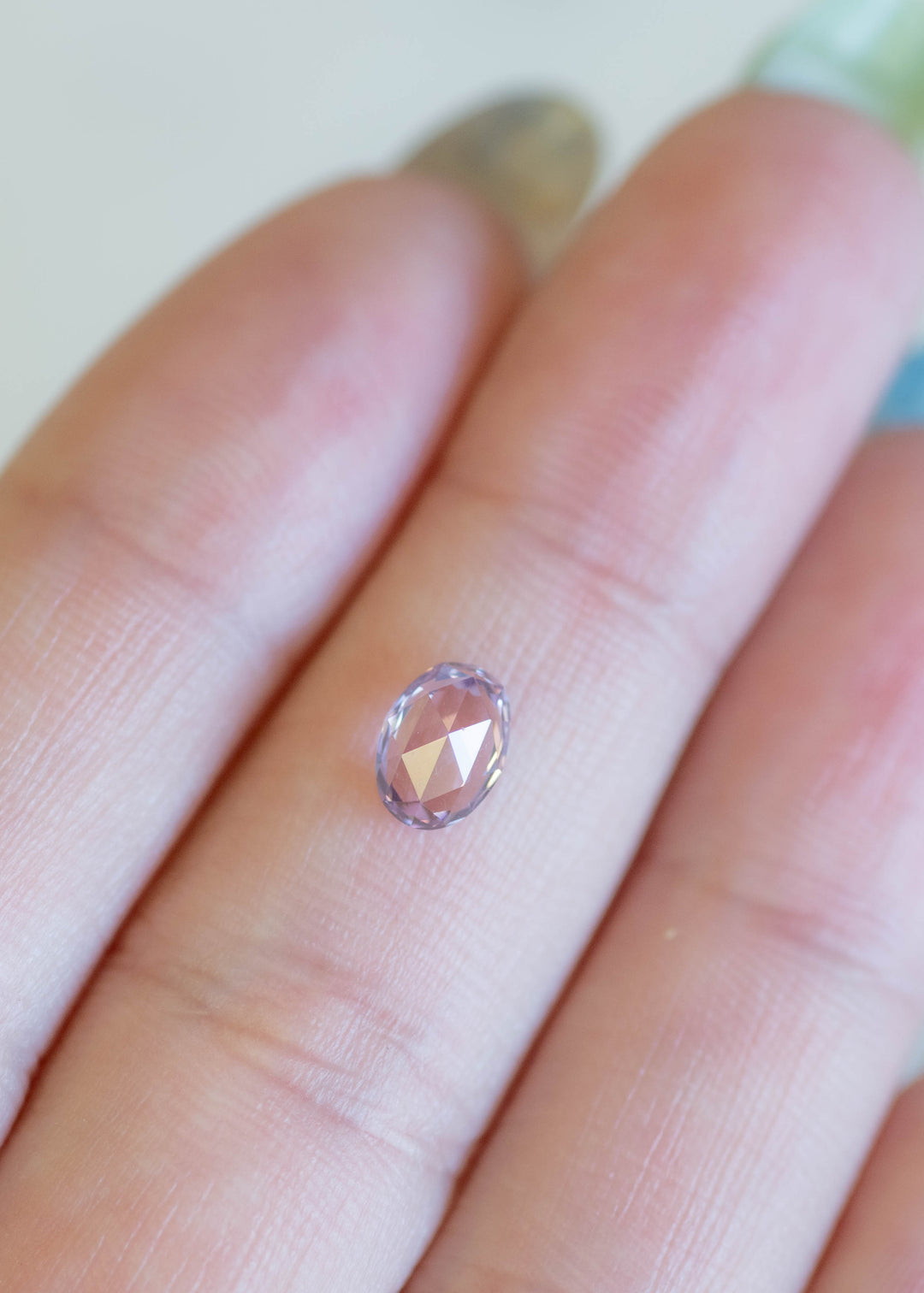 Oval rose cut lavender pink sapphire resting on fingertips, showing broad facet reflections and natural pastel color.