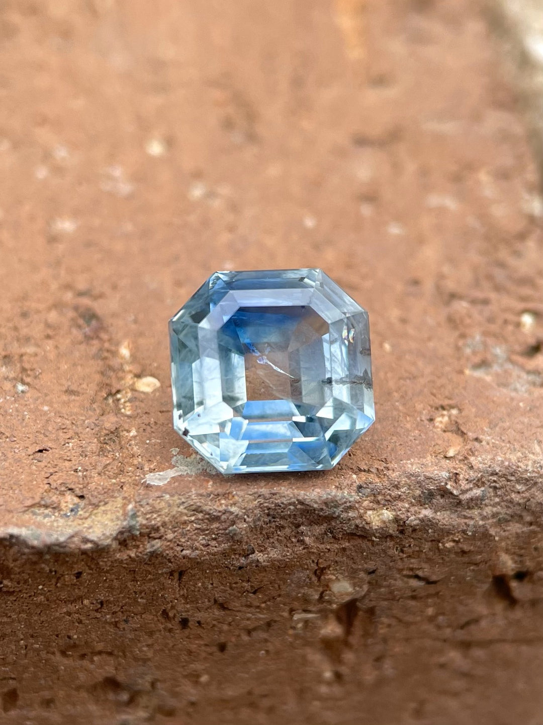 2.45-carat parti blue-green sapphire in an antique emerald cut, resting on a rustic, earthy brown surface, showcasing its exquisite step cut and vivid colors.