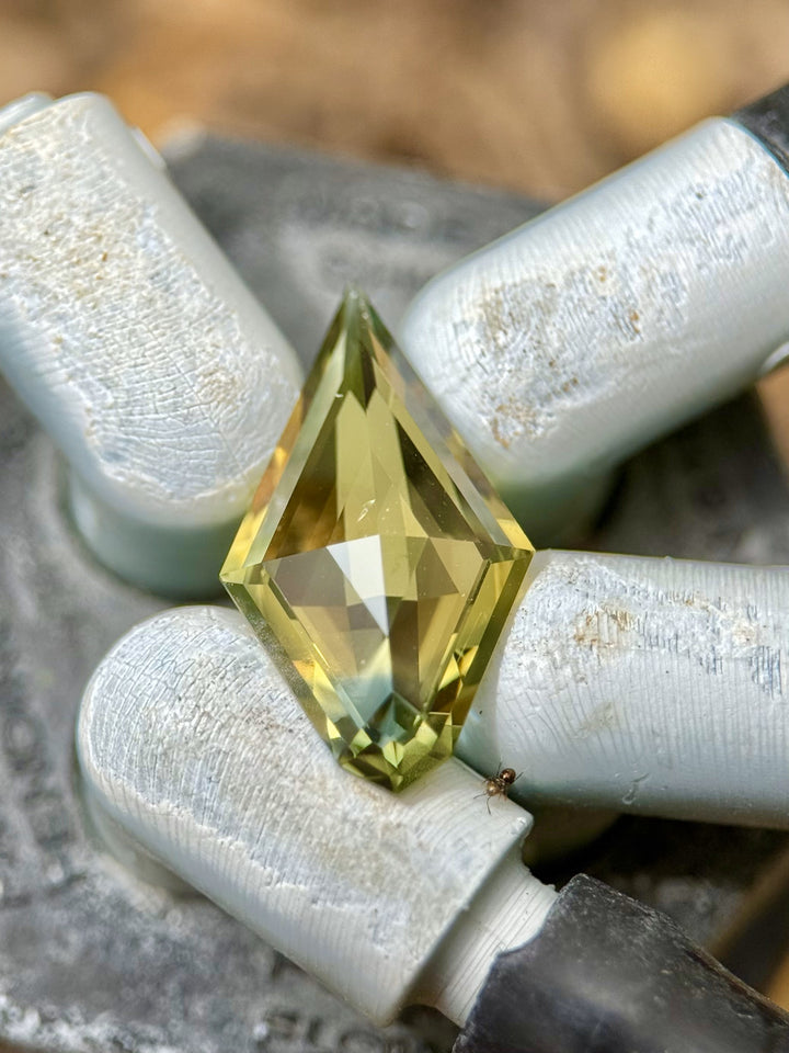 Macro photo of a 2.38-carat kite-cut parti sapphire in yellow and blue shades held in a gem dop tool, with visible cutting detail.