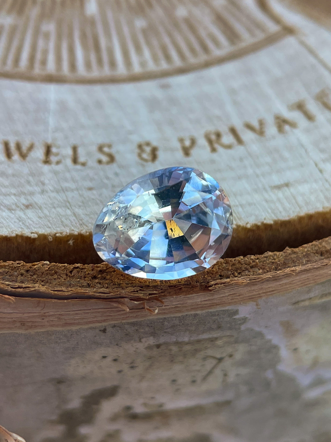 A stunning 1.95-carat Parti Yellow and Blue Sapphire in a pear-oval shape, unheated and ethically sourced from Sri Lanka. The gemstone is placed on a wooden surface with detailed craftsmanship in the background, highlighting its brilliance and color combination.