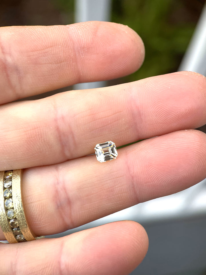 A pastel canary yellow sapphire, weighing 1.43 carats, displayed on a fingertip. The gemstone features an octagonal step cut, showcasing its radiant facets and delicate pastel hue, with natural lighting emphasizing its brilliance.