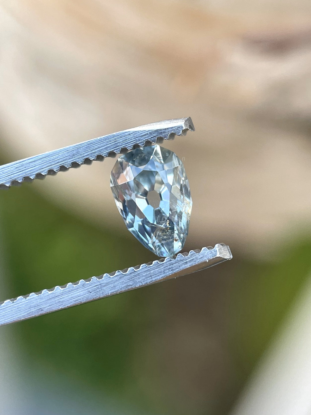Close-up of a 1.41-carat sapphire with a unique poval (pear oval) cut, held in tweezers. The gem displays yellow, blue, and green hues with brilliant sparkle. Ethically sourced from Chimwadzulu Hill, Malawi.