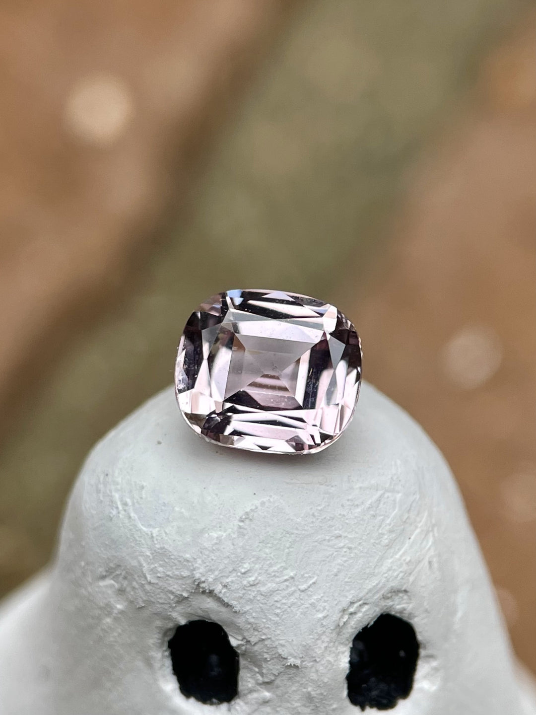 A cushion-cut sapphire with a pastel yellow and peach hue, weighing 1.19 carats, displayed on a ghost figurine. This gem features a modified cushion cut and is sourced from Sri Lanka. No treatment applied.