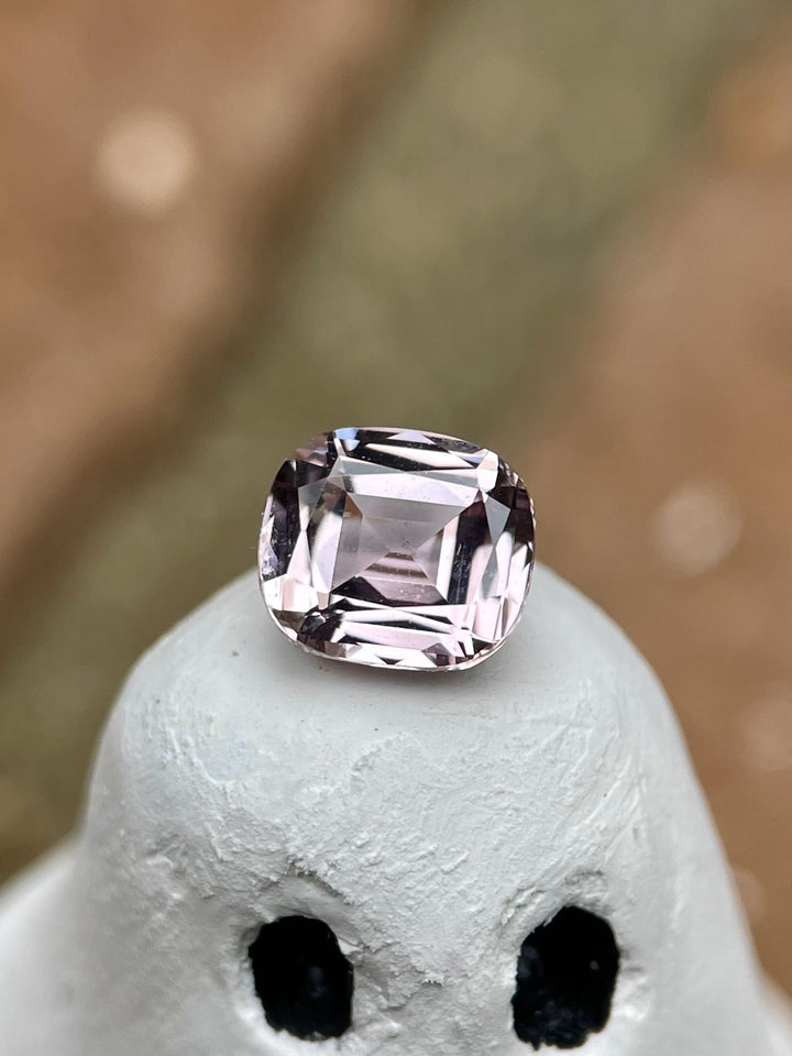 A cushion-cut sapphire with a pastel yellow and peach hue, weighing 1.19 carats, displayed on a ghost figurine. This gem features a modified cushion cut and is sourced from Sri Lanka. No treatment applied.