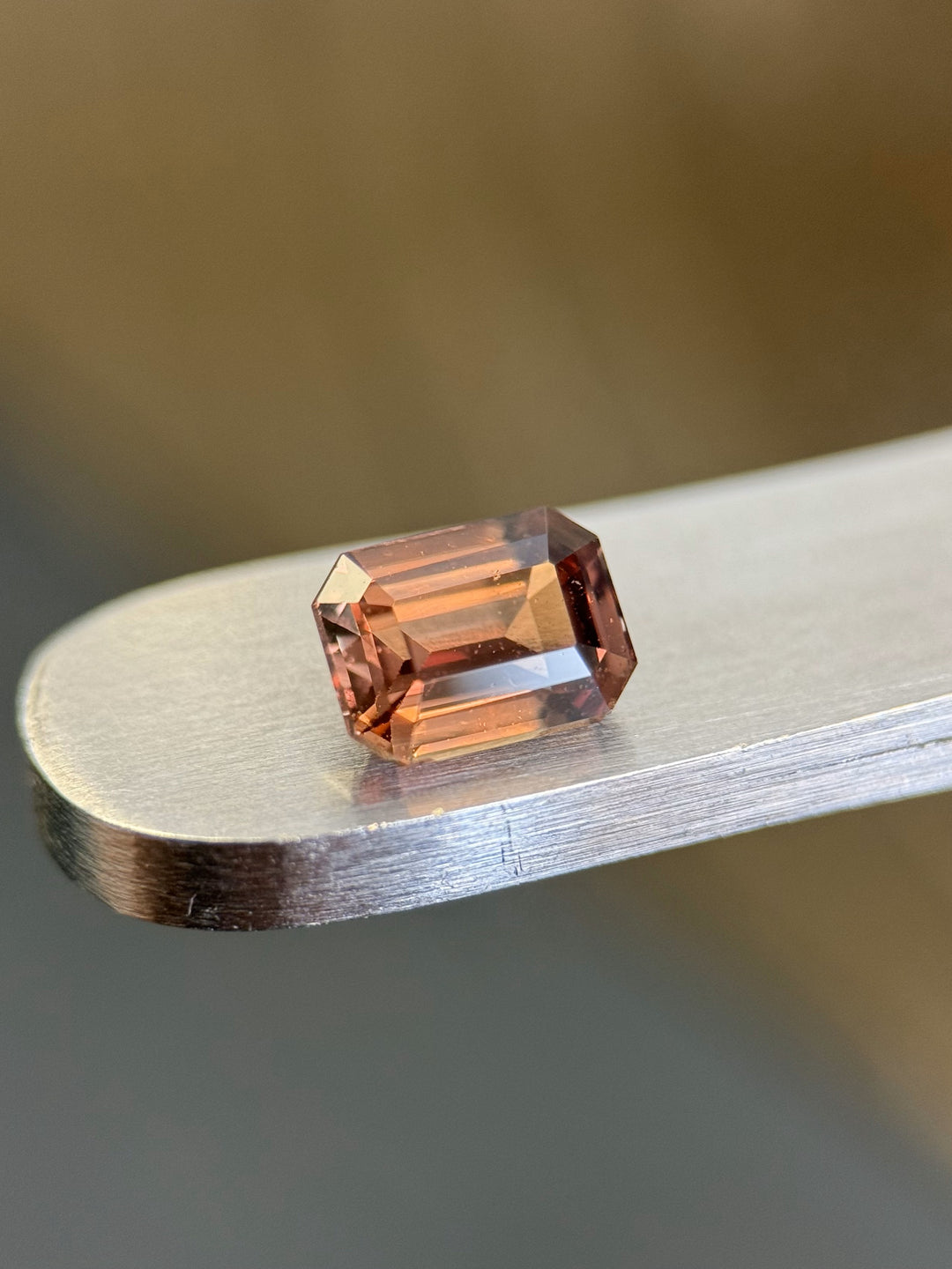 Close-up of a 1.10-carat unheated peac-pink sapphire with an emerald cut, displayed on a metallic surface.