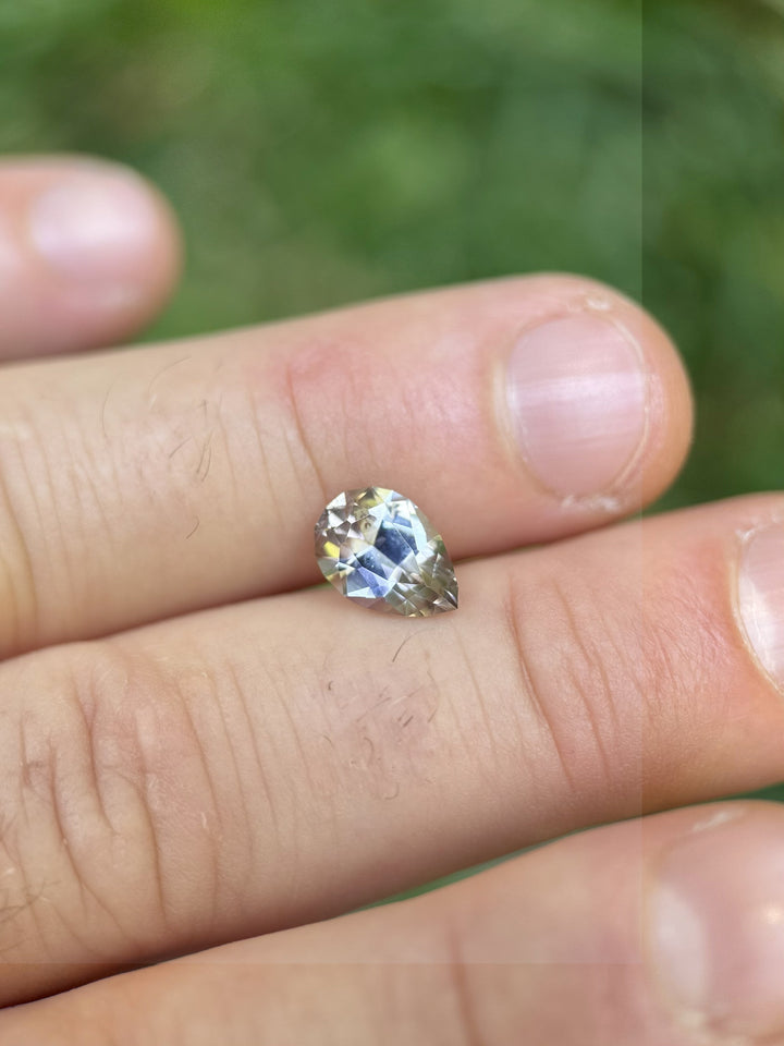 Peach-blue Tanzanite gem displayed on fingertips, highlighting its 2.19 carat size and radiant mixed cut sparkle