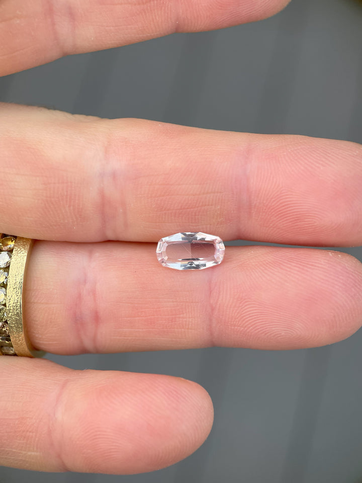 A 2.03-carat peach sapphire in a custom elongated step-cut portrait style, placed delicately on a hand. The gemstone exhibits its soft peach hues.