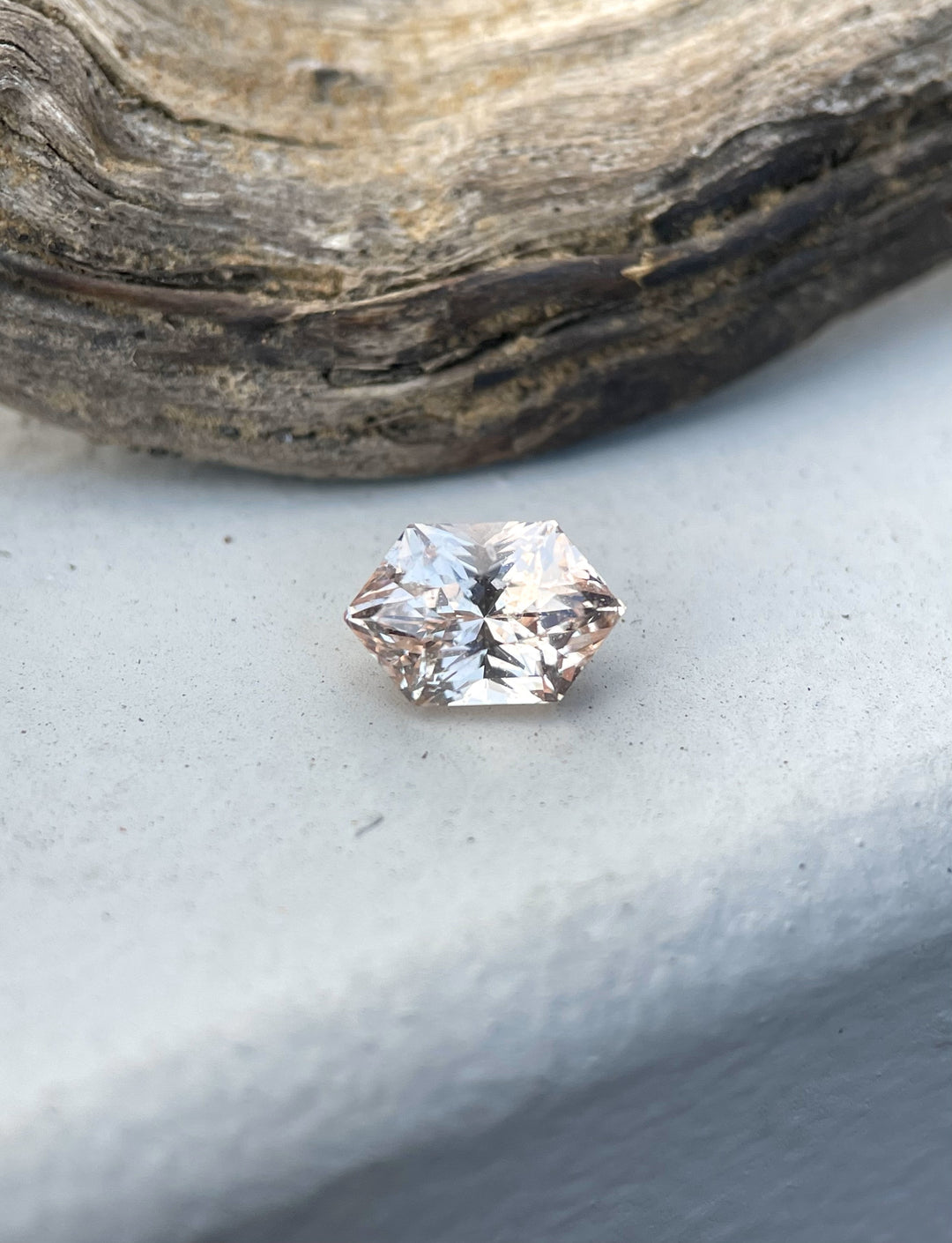 Peach champagne sapphire, 1.06 carats, resting on a rustic wooden surface, highlighting its unique hexagonal cut and brilliance.