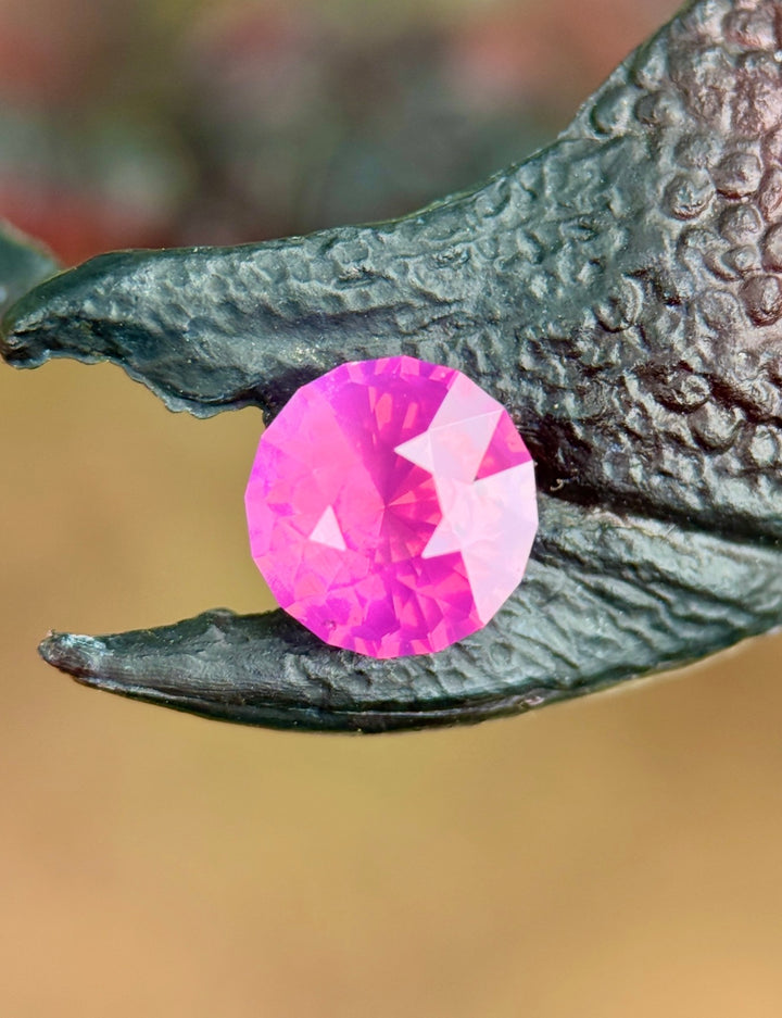 Loose pink opalescent sapphire from Sri Lanka displayed on textured surface highlighting the custom mix round cut and vivid pink tones.