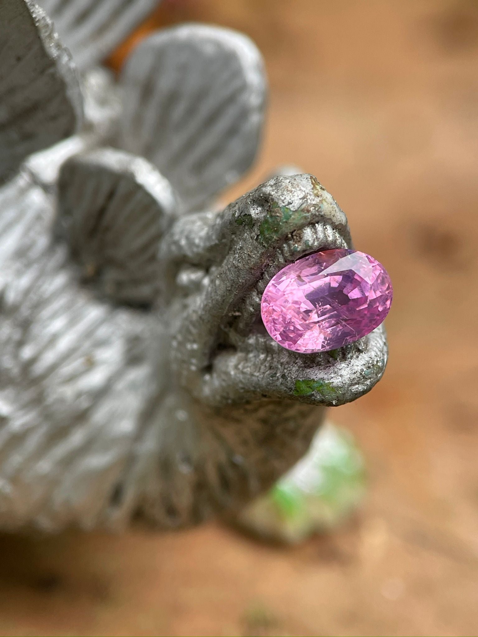 Pink oval cut loose sapphire on a decorative dinosaur sculpture, showcasing vivid color and one-of-a-kind character for custom jewelry.