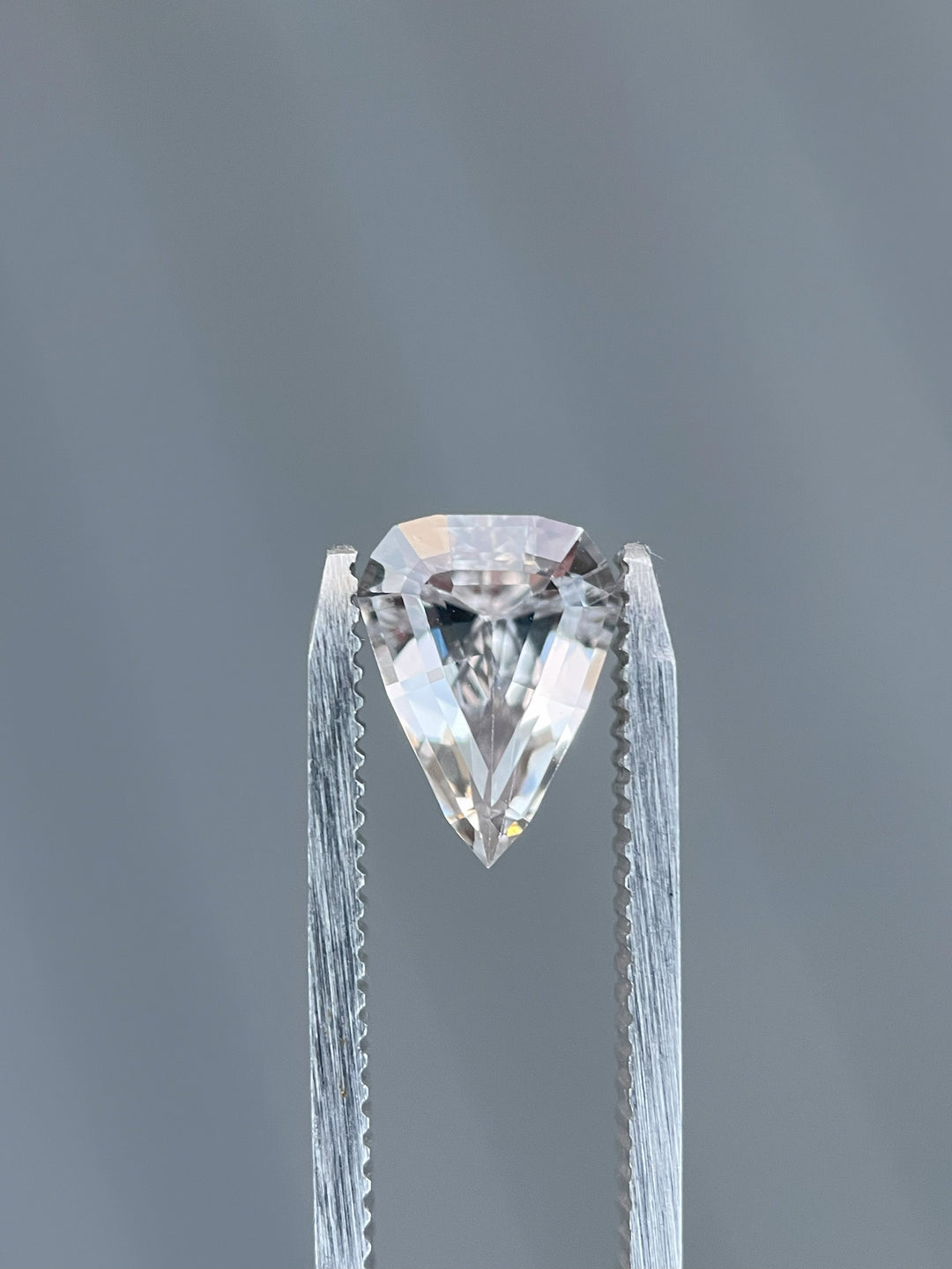 A natural sapphire transitioning from pink to peach tones, displayed in hand. The gemstone, cut in a modified geometric step cut shield, weighs 2.09 carats and originates from Sri Lanka.