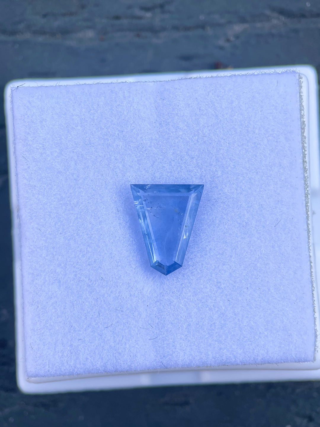 Exquisite 1.62 carat sapphire in a custom geometric portrait cut, showcasing a delicate blend of powder blue and denim blue. This parti-colored gem measures 10.32mm by 8.35mm, set against a serene backdrop, highlighting its fine cut and clarity from Sri Lanka, untreated.