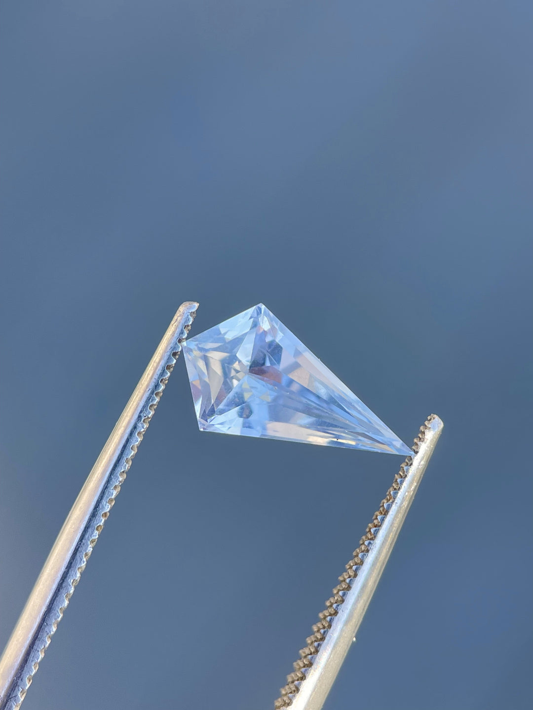 Close-up of a 1.66 carat sapphire, displaying its unique geometric step cut kite shape and subtle periwinkle to powder blue color transition, elegantly positioned against a soft backdrop.