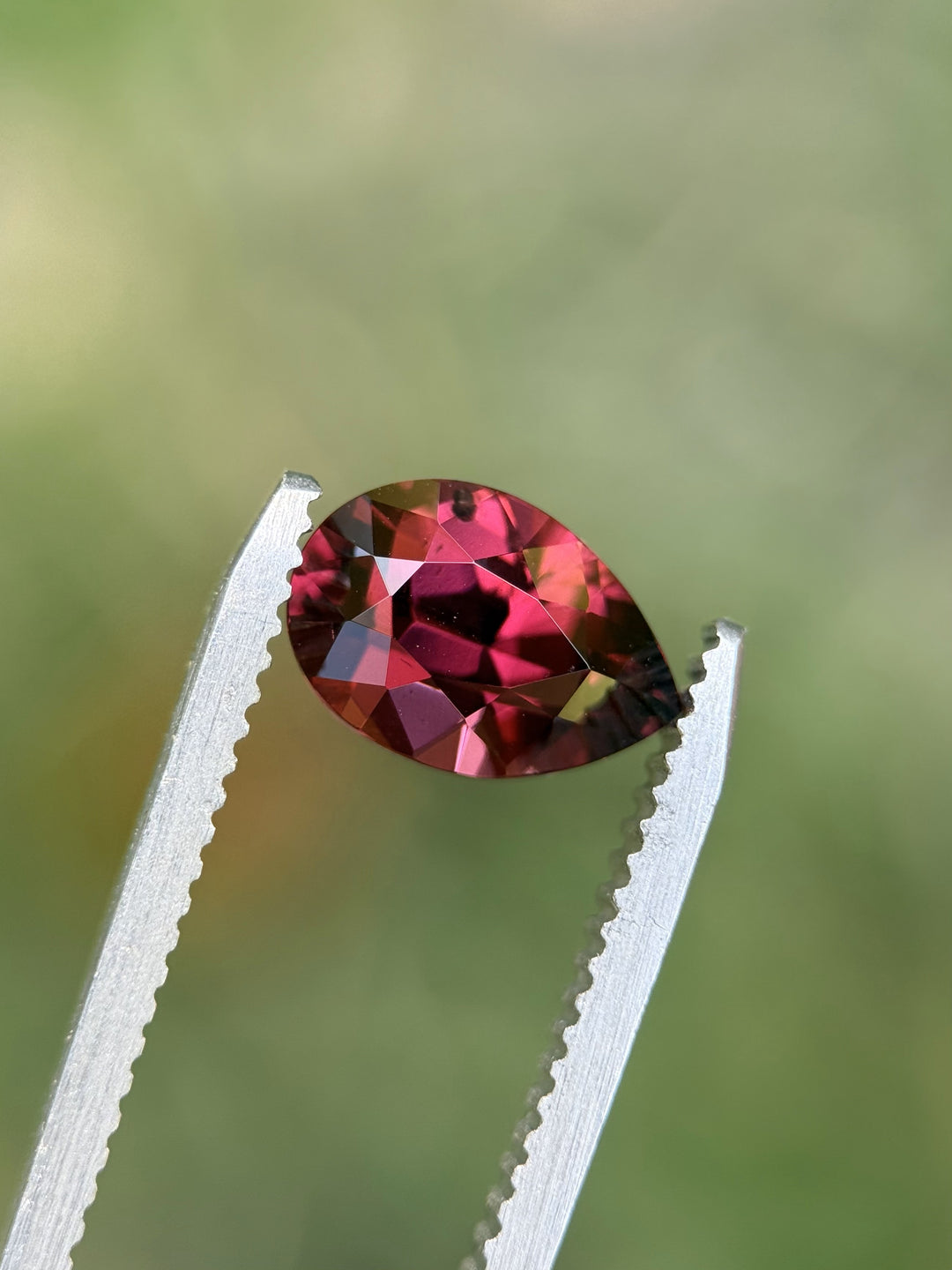 Close-up of 2.40CT rose red garnet held in tweezers against soft background, highlighting clean facets and precision cutting