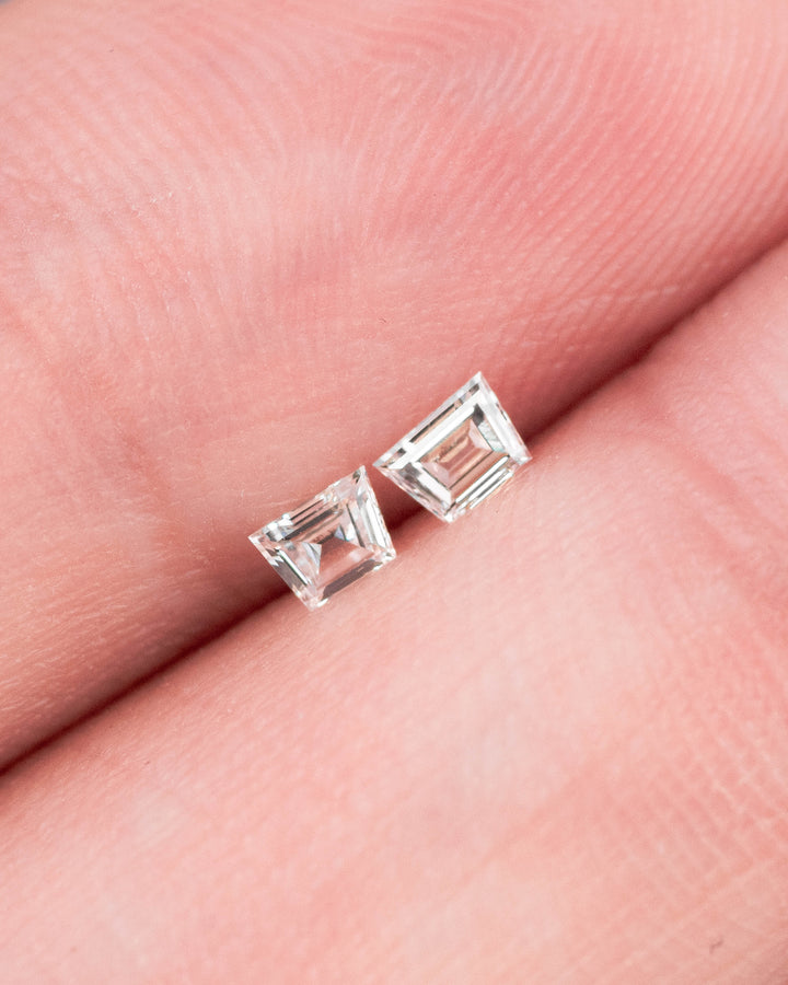 Matched pair of 0.18 carat F-G color VVS clarity Trapezoid step cut diamonds resting on fingertips, showing the size, brilliance, and clean faceting of the precision-cut South African diamond pair.