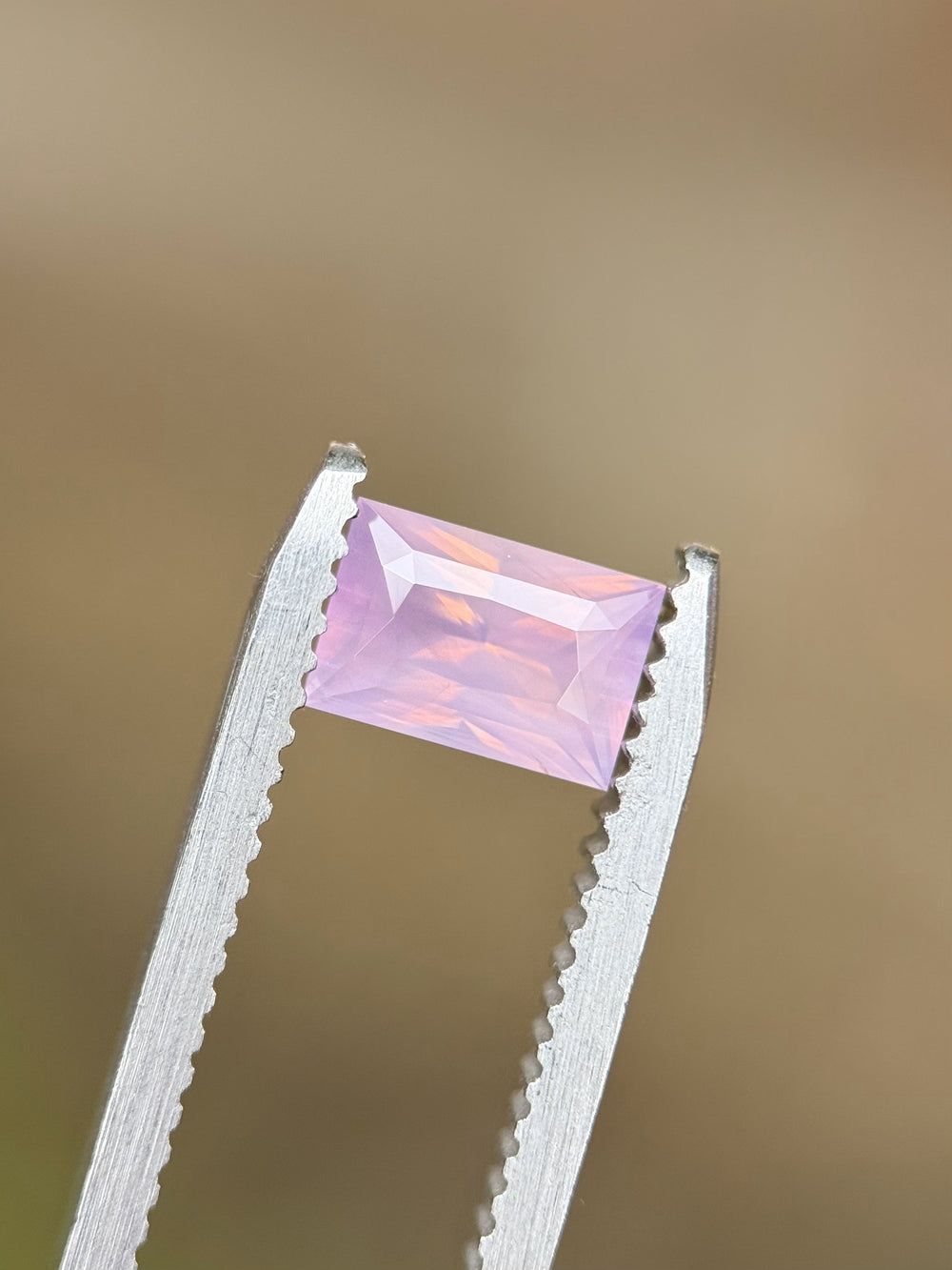 Close-up of untreated blush pink sapphire held by tweezers, showcasing precision baguette mixed cut facets.