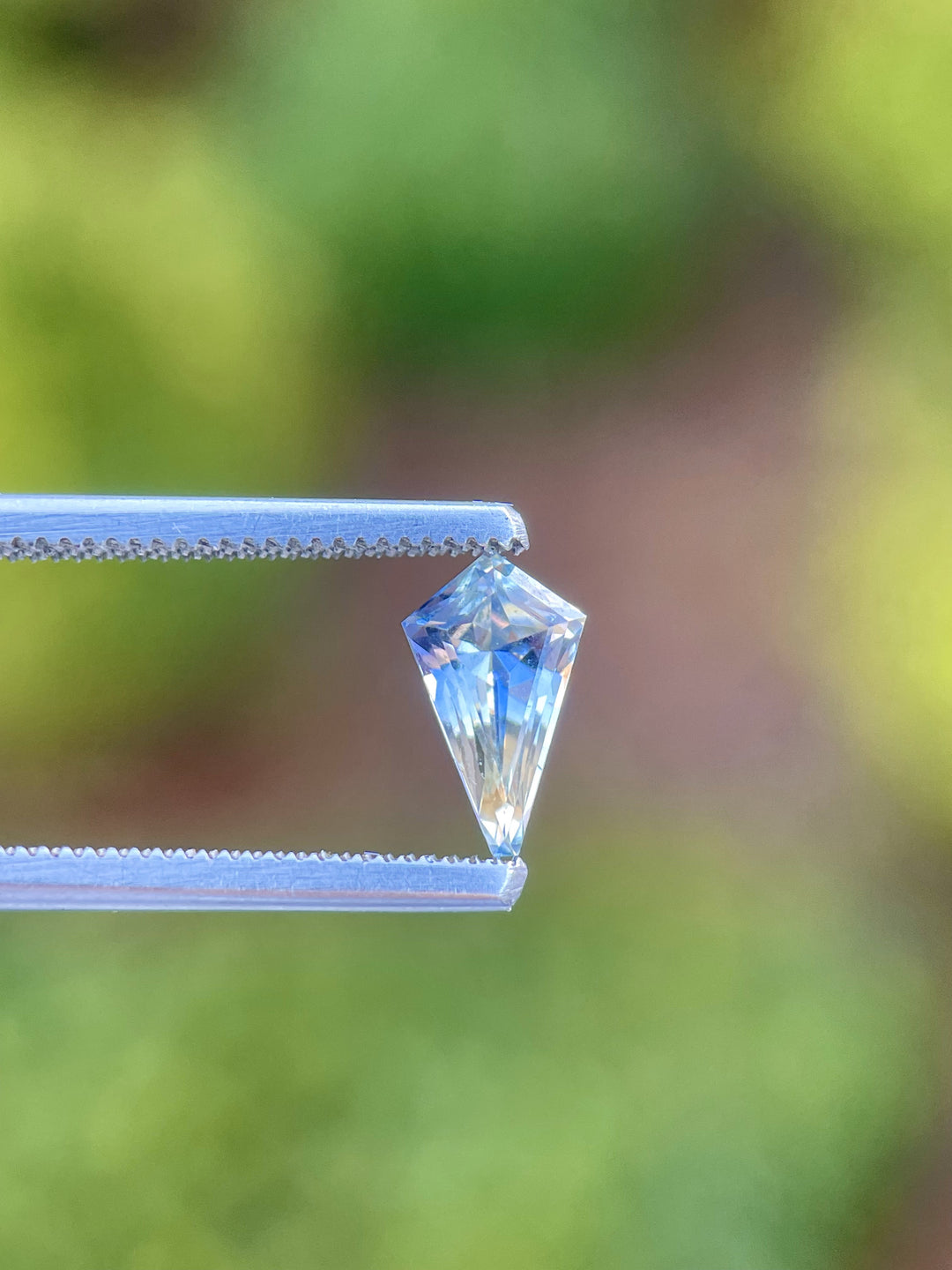 Close-up view of a 1.20 carat parti-colored sapphire held in tweezers, showcasing its unique yellow and cornflower hues and custom kite cut, highlighting its natural origin from Sri Lanka.