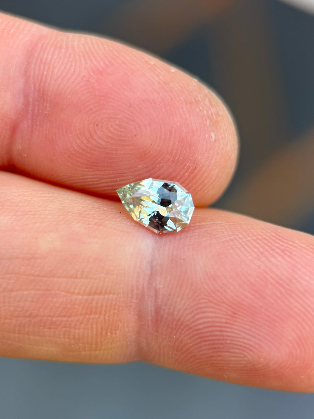 Precision pear cut sapphire resting on fingertips, showing delicate seafoam green color and lively facet reflections.