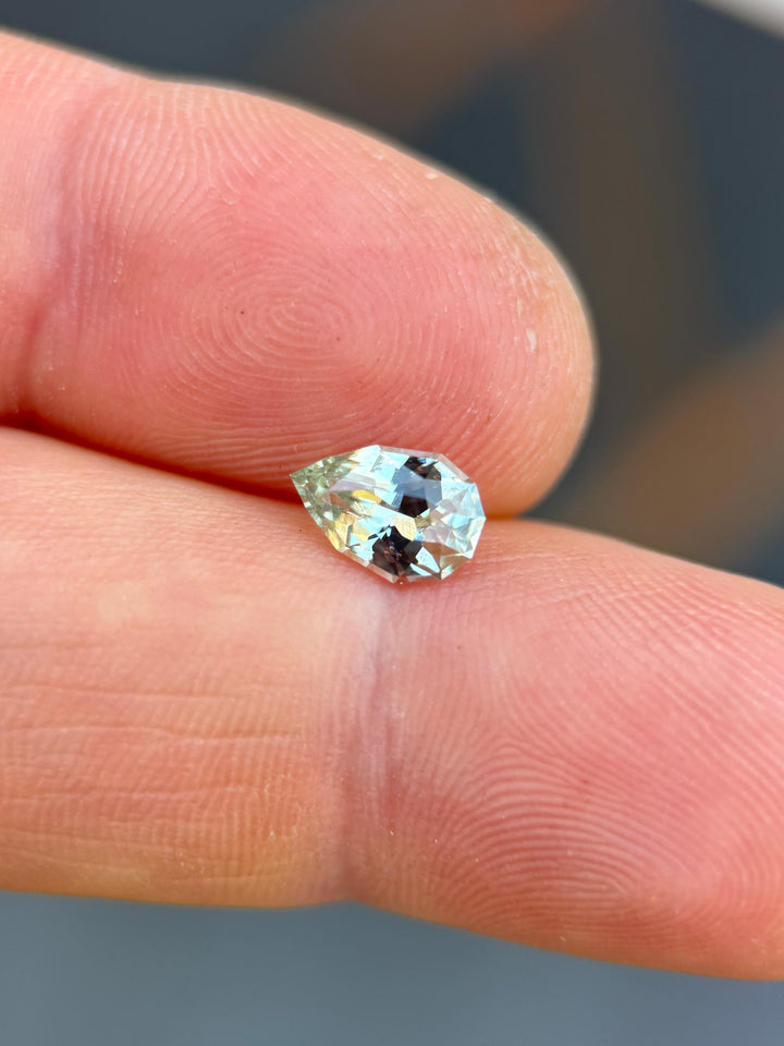 Precision pear cut sapphire resting on fingertips, showing delicate seafoam green color and lively facet reflections.
