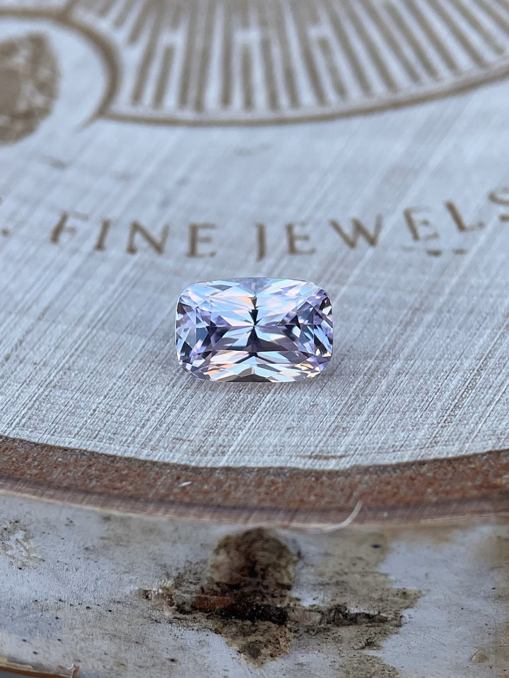 1.57-carat pastel pink and purple sapphire with a rectangular cushion brilliant mixed cut, ethically sourced from Sri Lanka, displayed against a fine wood backdrop.