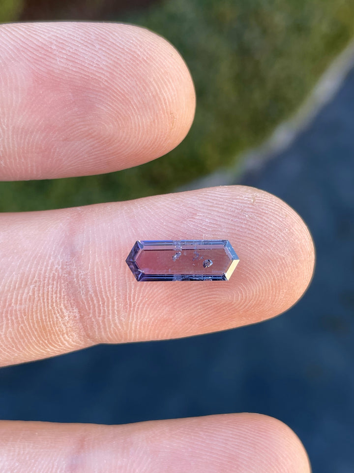 Close-up image of a purple and pink hexagonal step cut spinel gemstone weighing 1.82 carats, showcasing its transparent clarity and step-cut facets.