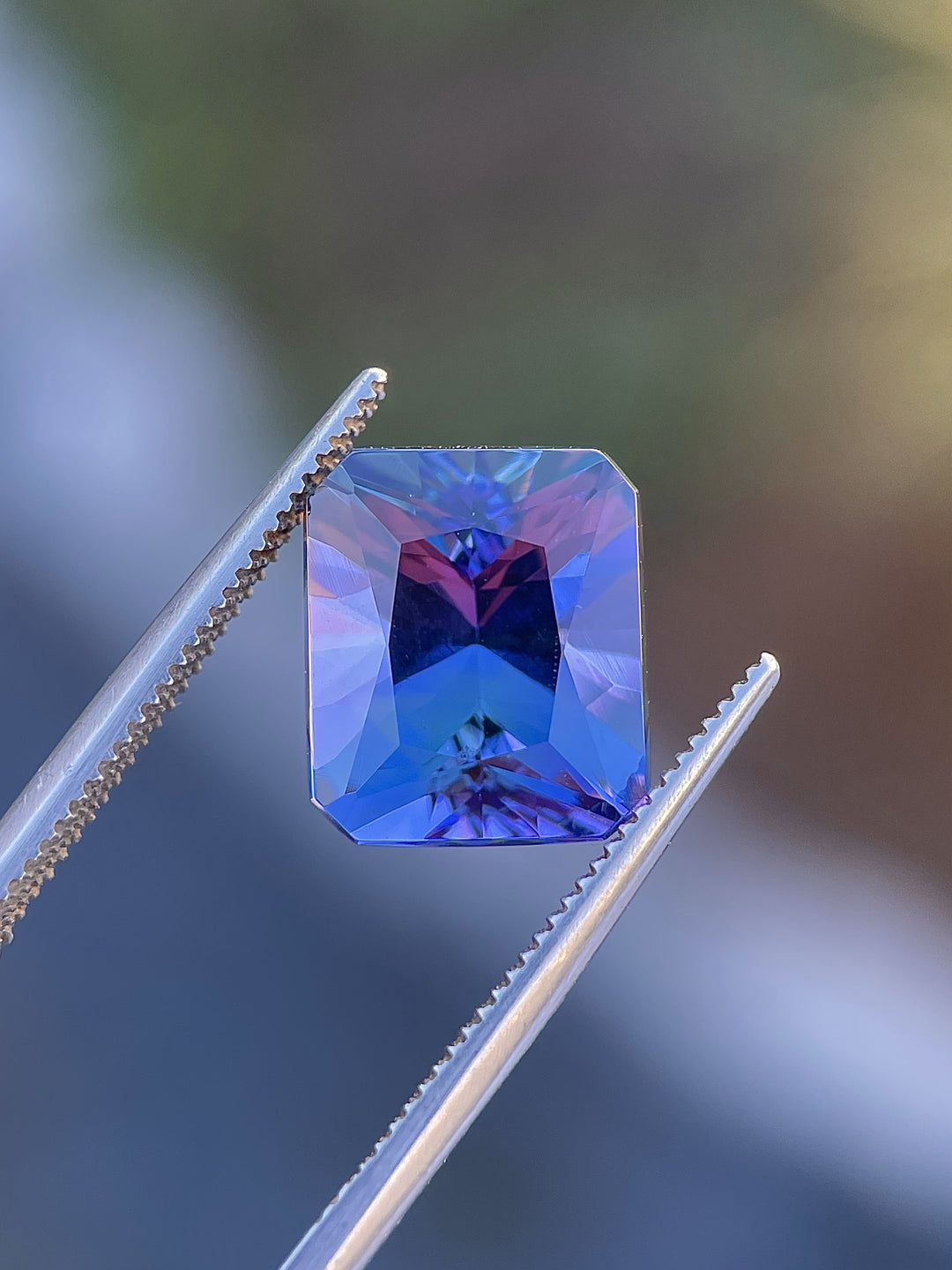 Tanzanite gemstone with a radiant-cut design, weighing 7.24 carats, held by precision tweezers against a gradient background.