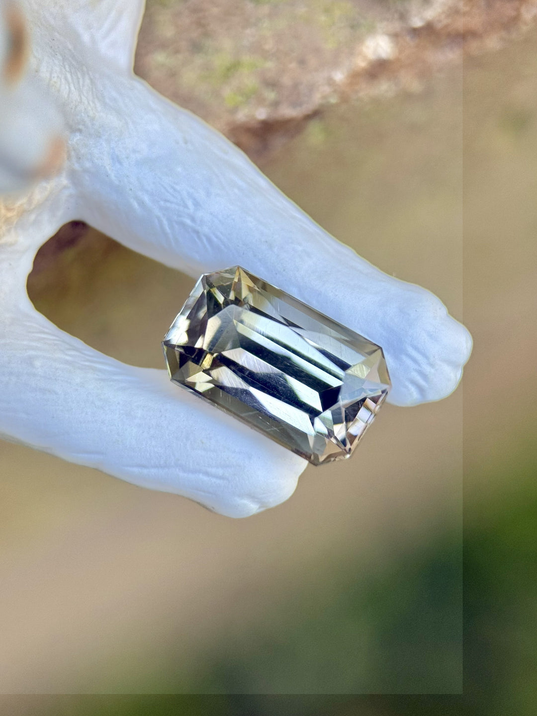 2.32 carat custom radiant tanzanite gemstone displayed on white coral hand, showing grey, teal, and blue hues – Merelani Hills, Tanzania