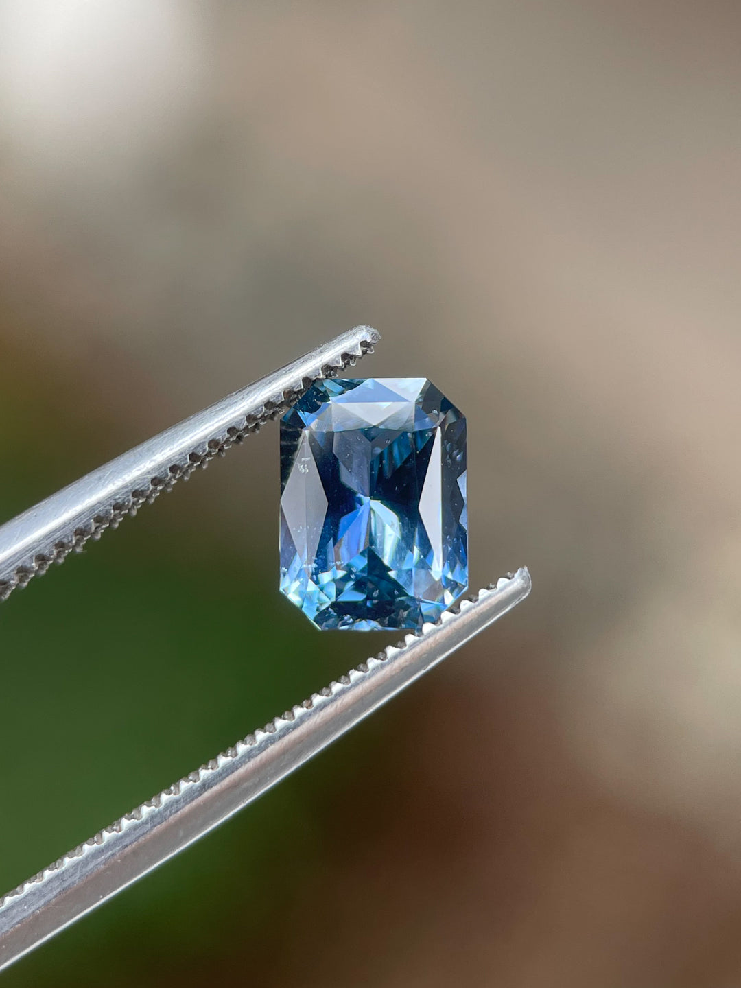 A radiant-cut blue sapphire weighing 1.54 carats, held with precision, highlighting its vivid colors and heated origin from Sri Lanka.