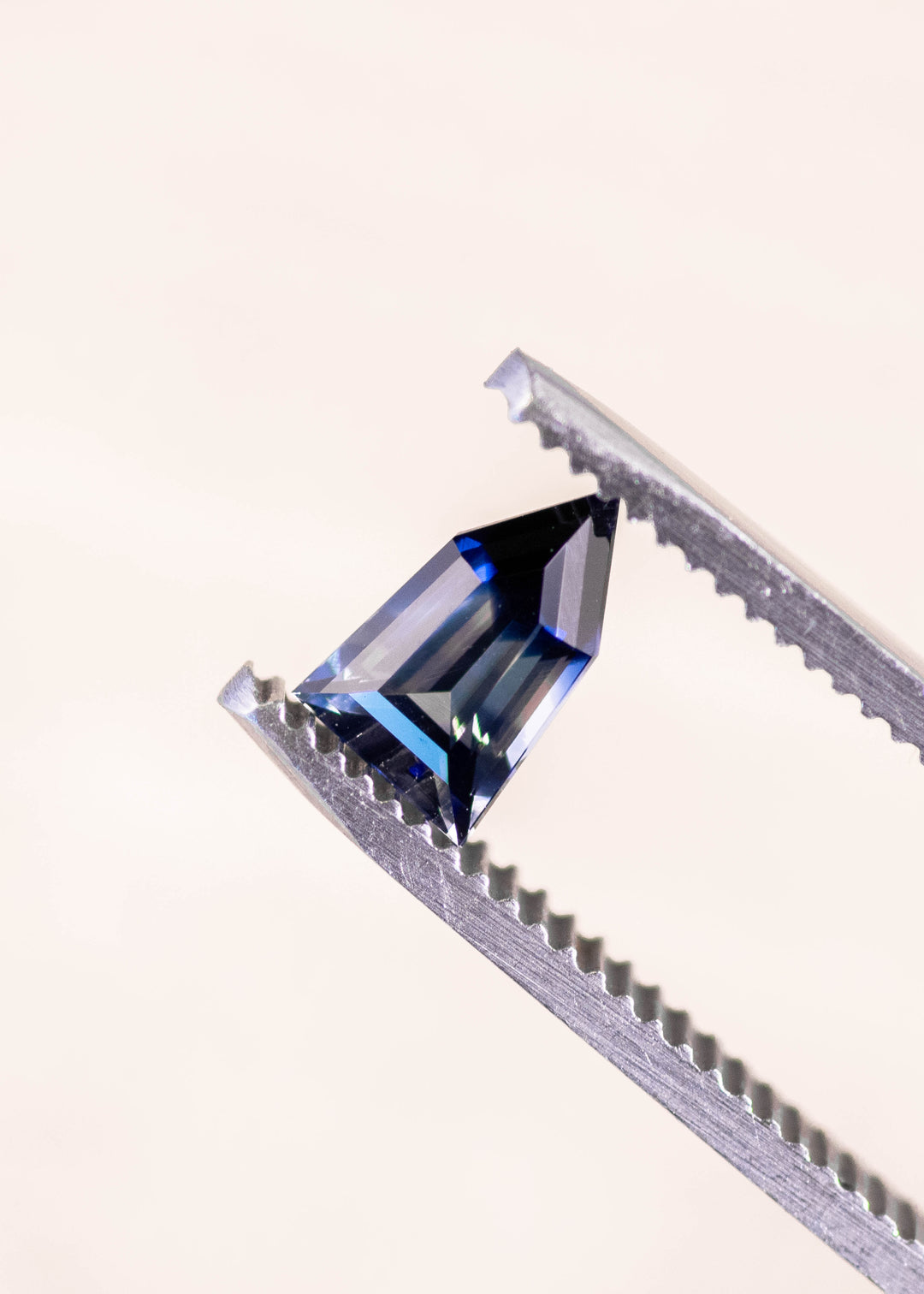Bi-color colorless blue sapphire held in gem tweezers, showcasing sharp pentagon shield step cut facets and clean color zoning, 1.22ct untreated sapphire from Sri Lanka