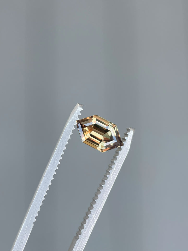 A beautifully faceted 1.22-carat sapphire from Songea, Tanzania, featuring a unique hexagon step cut and natural earthy tones of brown, orange, and pink.
