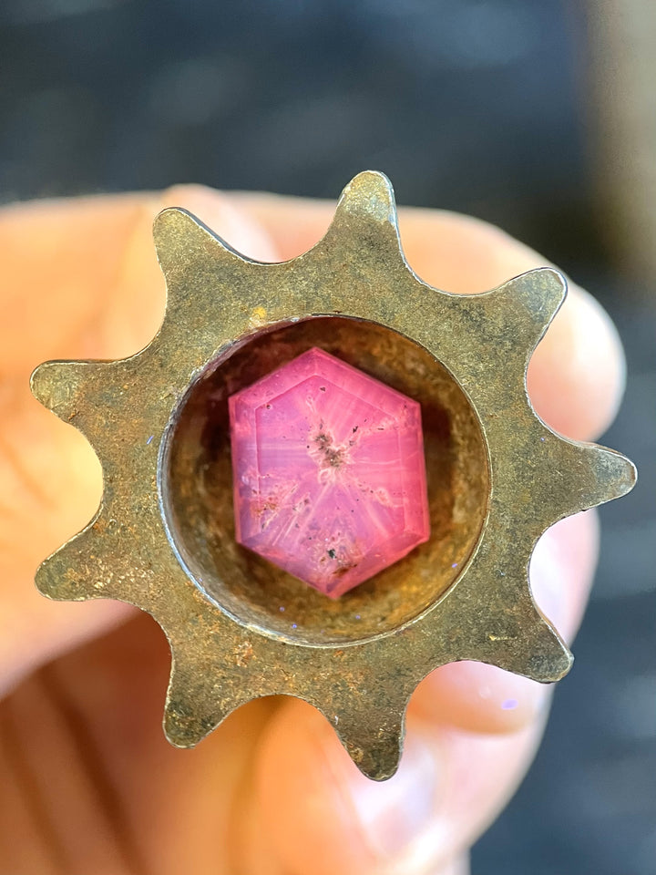 A close-up of a 19.62-carat pink and purple sapphire, capturing its unique hexagon portrait cut and naturally occurring inclusions in a metallic setting.