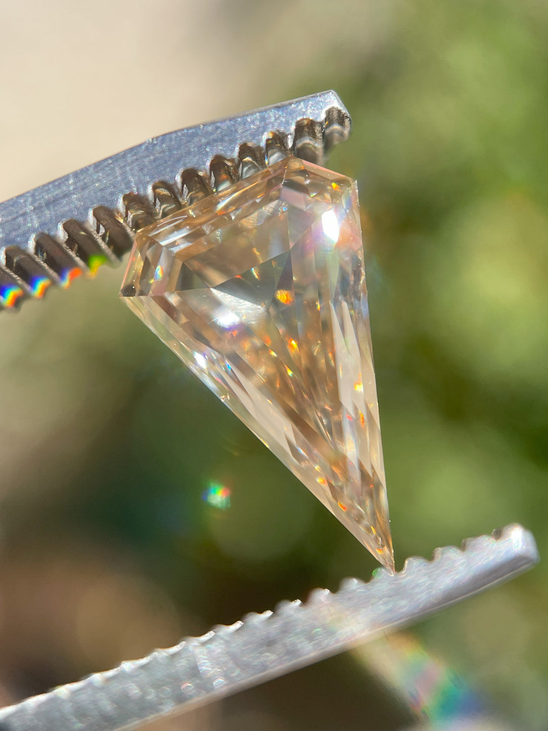 Macro shot of a 2.10ct rosy champagne diamond held in tweezers, displaying intricate faceting and fiery brilliance under natural light.