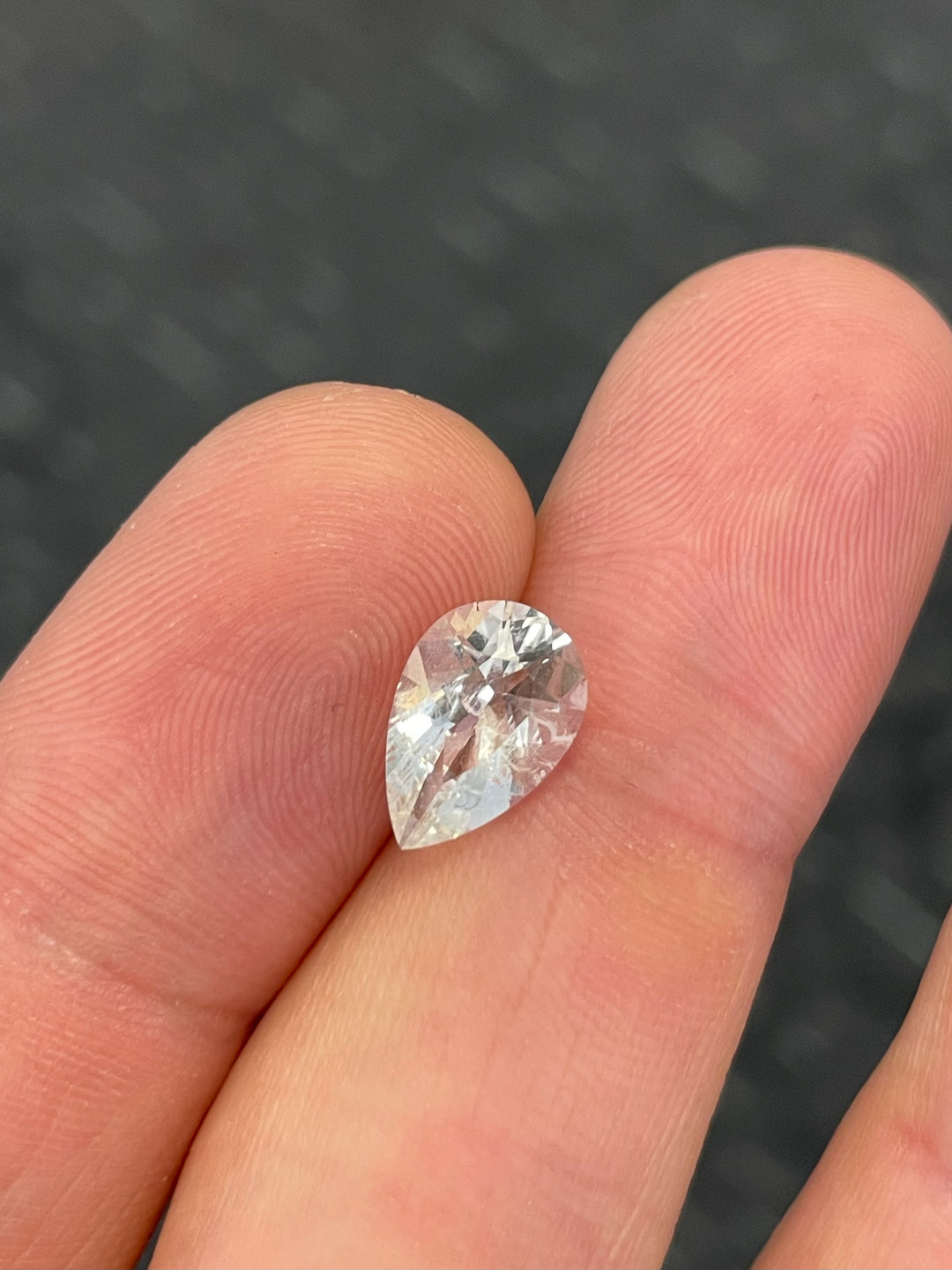 A 2.30-carat pear brilliant-cut hyalite opal held between fingers, showcasing its colorless clarity and intricate faceting.