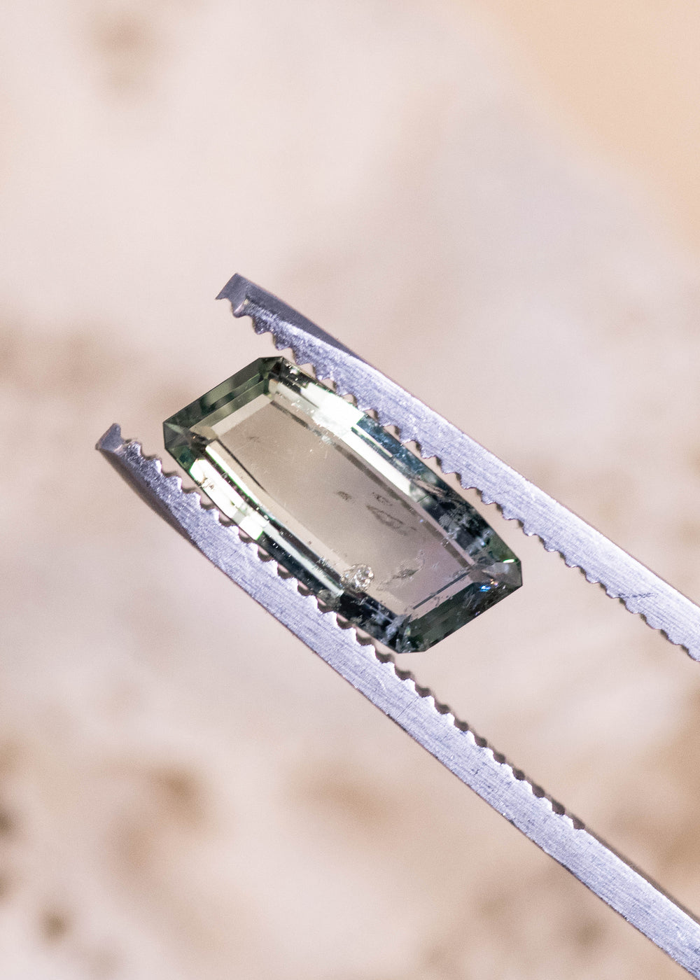 2.31 carat yellow green teal sapphire held in gem tweezers, displaying precision step-cut facets and elongated baguette portrait shape from the Umba River, Tanzania, untreated