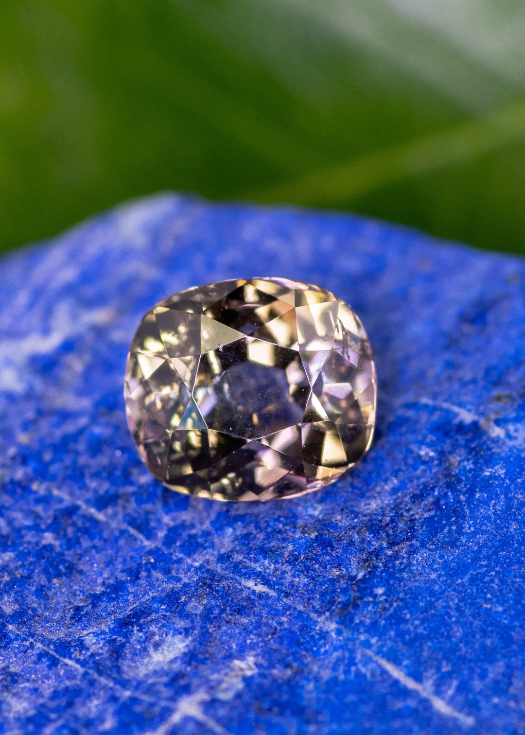 3.27 carat natural tanzanite in a custom modified old mine cut resting on a blue mineral background, showing purple, pink, and peach color zoning with soft antique-style faceting, untreated gemstone from Merelani Hills Tanzania