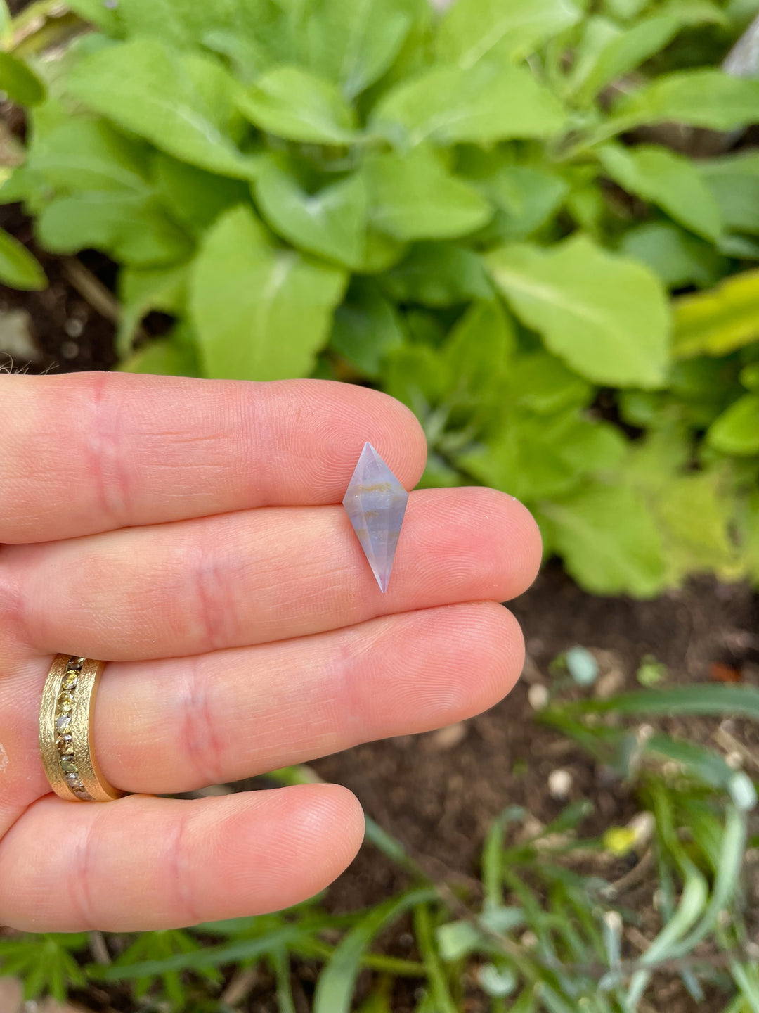 Close-up of 8.00 carat periwinkle sapphire with earthy zoning patterns and a precision rhombohedral cut, photographed outdoors.