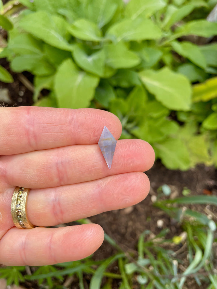 Close-up of 8.00 carat periwinkle sapphire with earthy zoning patterns and a precision rhombohedral cut, photographed outdoors.