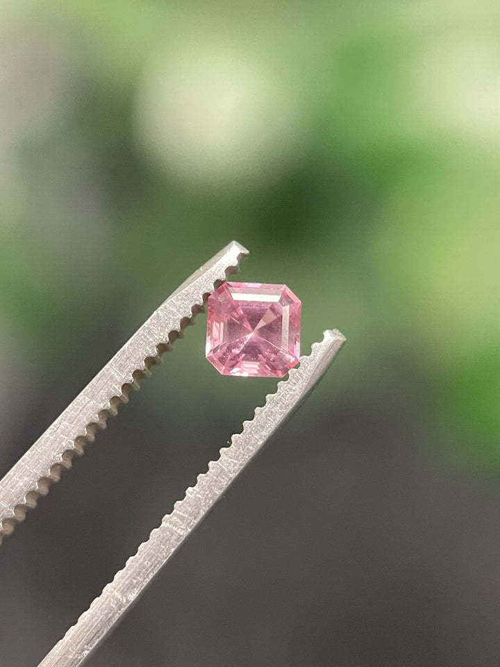 A 0.56ct Montana sapphire in an octagonal step cut, delicately held by gem tweezers against a blurred green background.