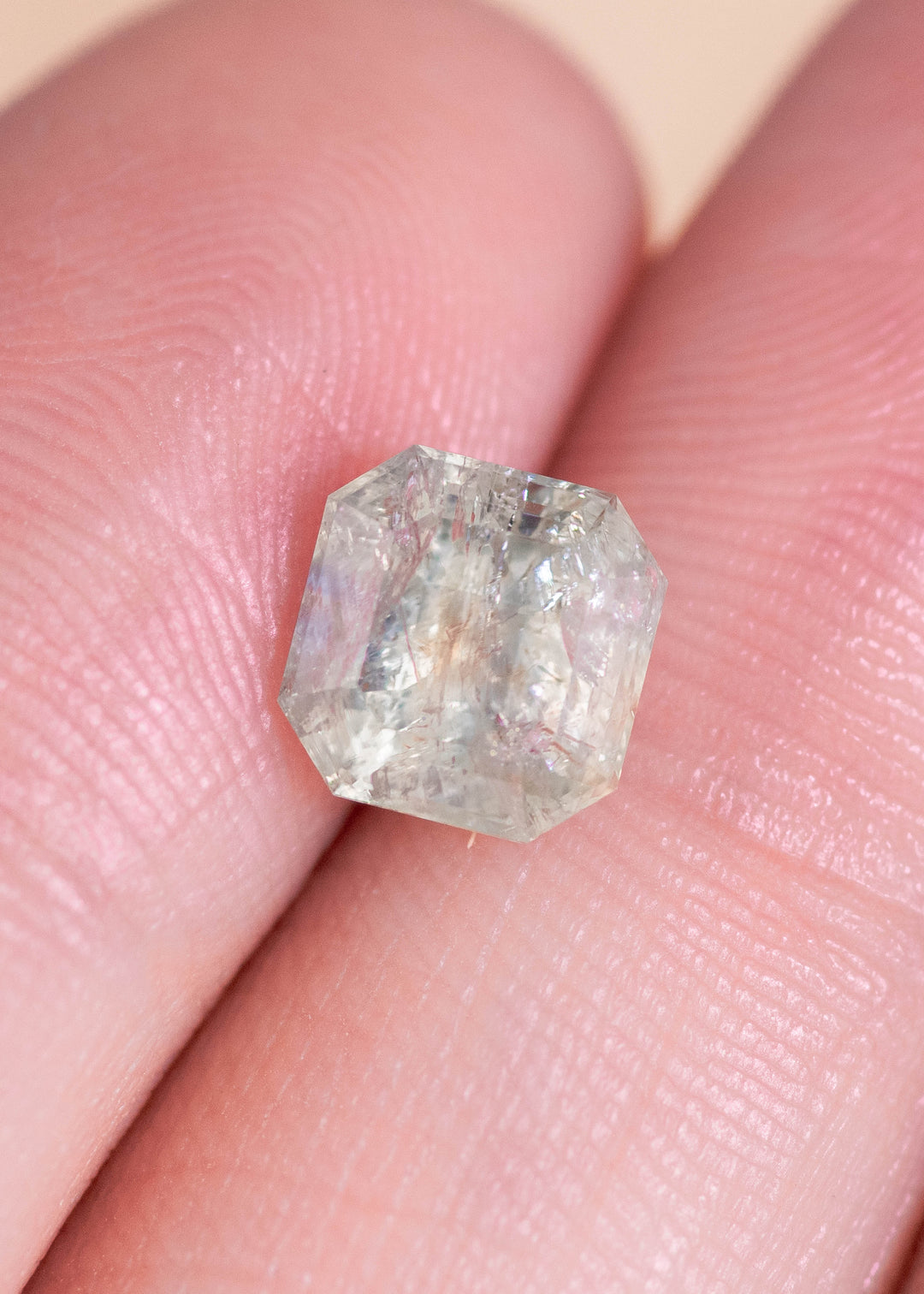 Natural 2.25CT seafoam teal sapphire displayed on fingertips for scale, highlighting the Asscher cut geometry, untreated Montana origin, and visible internal crystal features under soft natural light.