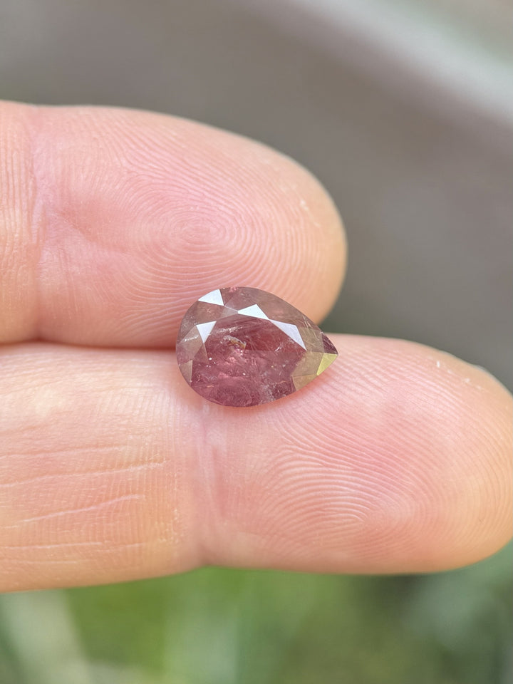 Close-up of 3.75ct earthy red-orange Umba River sapphire resting on fingertip, showing pear shape and natural inclusions