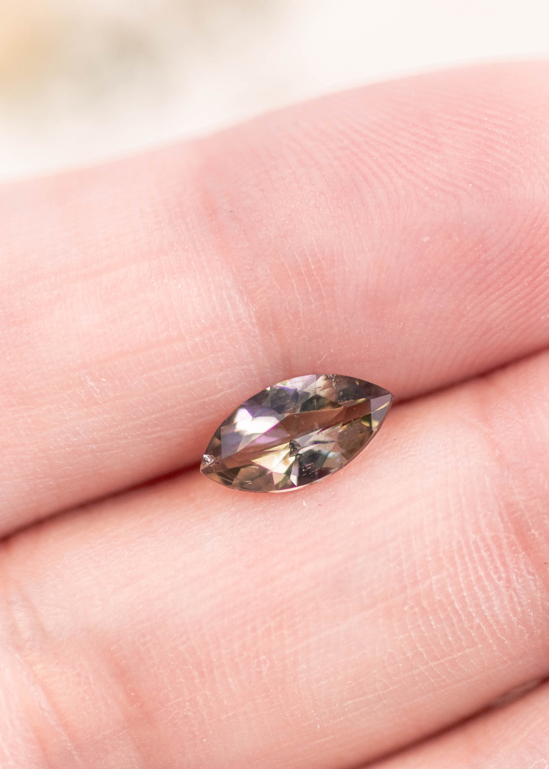 1.00 carat yellow-teal-green tanzanite marquise cut resting on a fingertip to show scale, depth, and brilliance of the untreated gemstone from Merelani Hills, Tanzania